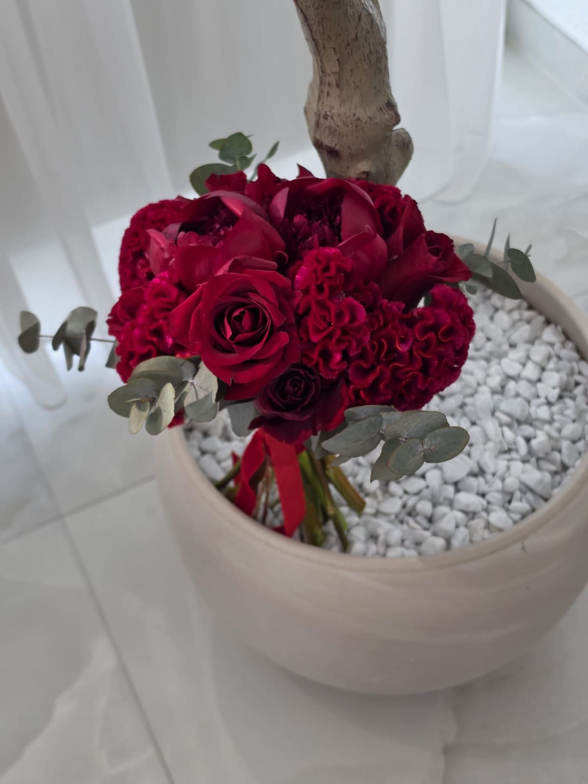 Roter Brautstrauß aus Rosen und Celosien in einer Schale mit weißen Kieseln